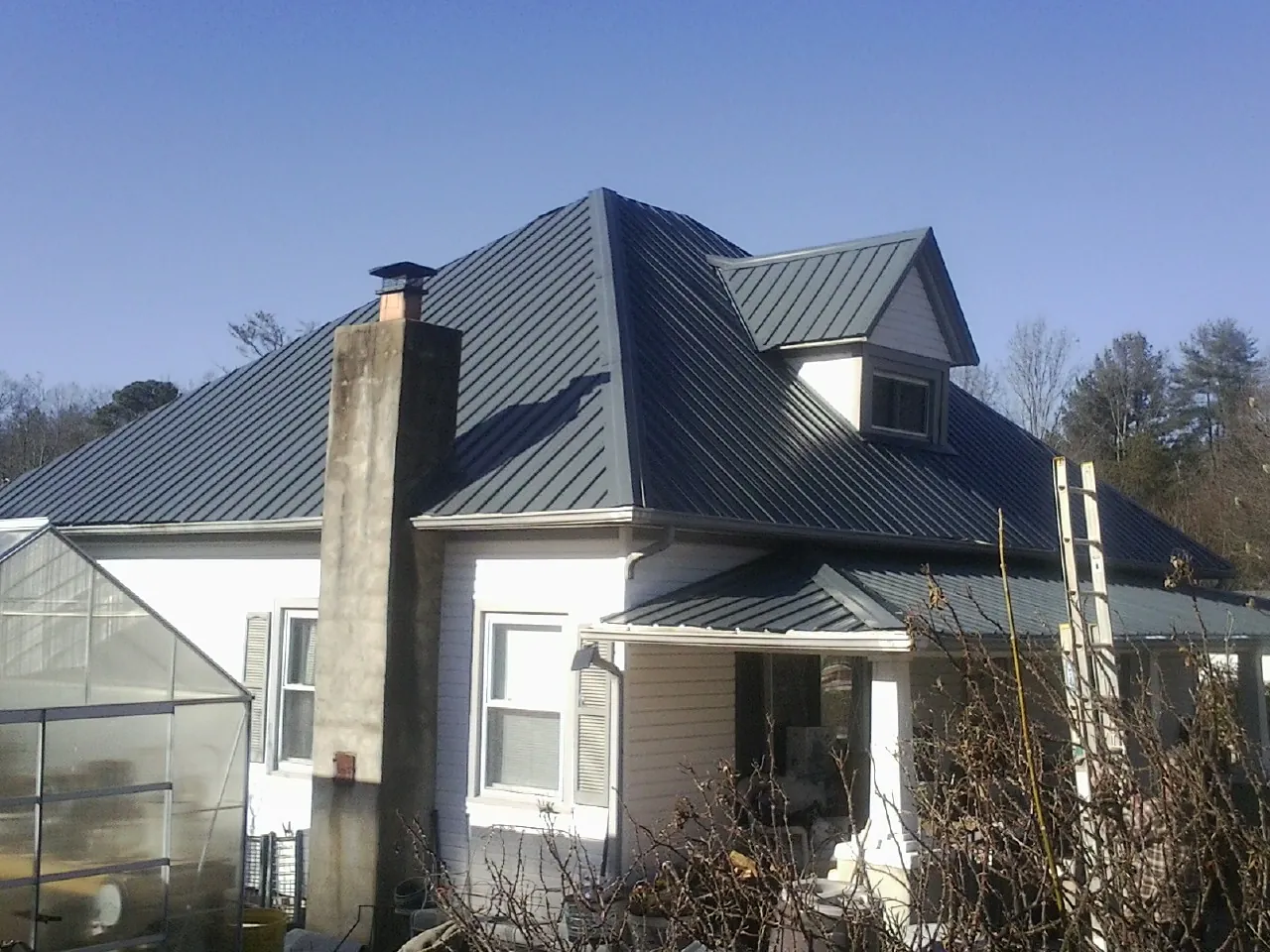 Dark blue standing seam metal roof on a white farmhouse with dormer — Slate & Tile Roof Repair by Roofing Brothers in Muskego