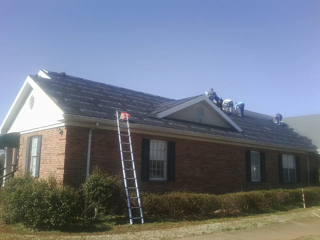Crew tearing shingles off a brick ranch roof with a ladder set — Metal Roof Repair work by our crew in Muskego