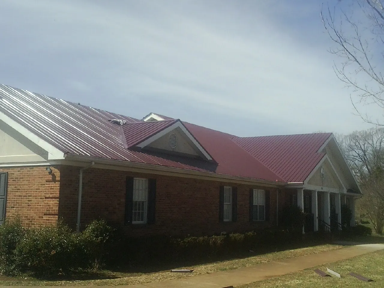 Red metal roof with gabled entries on a long brick building, from a Hail Damage Roof Repair job in Muskego