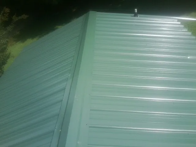 New green metal panels meeting at the ridge of a roof — Flat Roof Repair work by our crew in Muskego