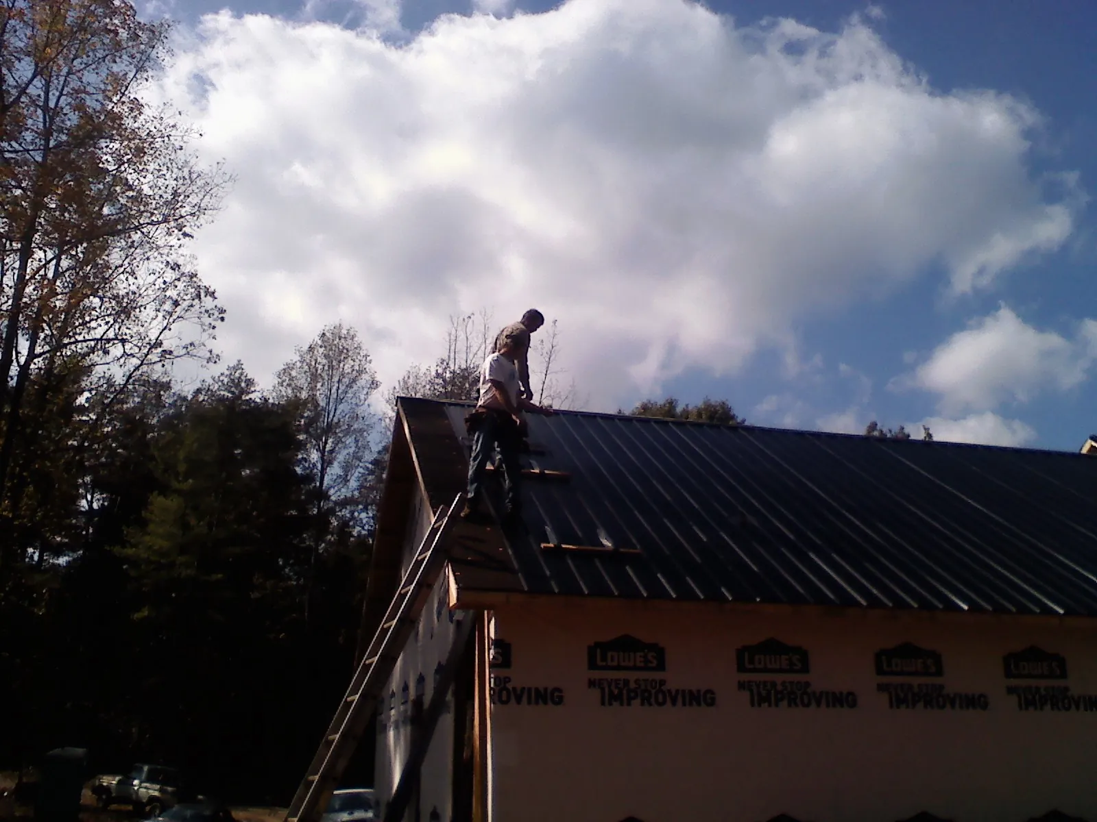 Roofer fastening dark metal panels high against a cloudy sky, from a Roof Inspection job in Muskego