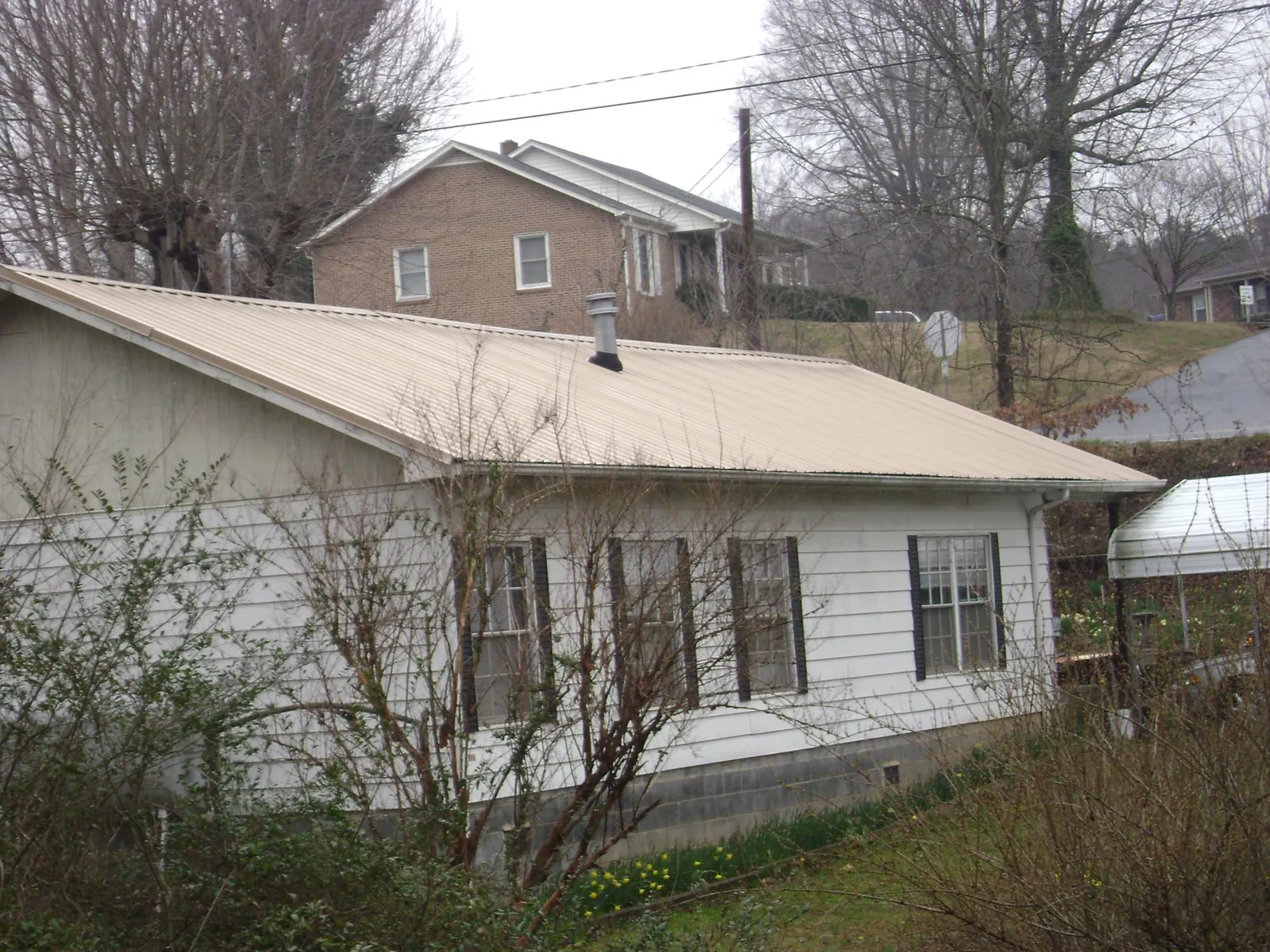 Tan metal roof on a white sided house set into a hillside — Commercial Roofing by Roofing Brothers in Muskego